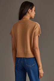 A woman stands with her back to the camera against a plain gray background, wearing the Panache Apparel Collection Light Brown Short Sleeve Sweater, paired with blue jeans, hoop earrings, and gold bracelets.