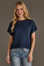 A person with long blonde hair is wearing the Panache Apparel Collection Navy Short Sleeve Sweater and light blue jeans, standing against a plain gray background and smiling gently at the camera.