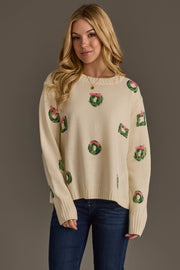 Woman wearing the Ivory Wreath Sweater with Pink Bows, a cream-colored crewneck sweater featuring a pattern of green wreaths with pink bows.