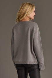 A person seen from the back wearing a long-sleeved, gray Gray Tis The Season Sweater and black pants.