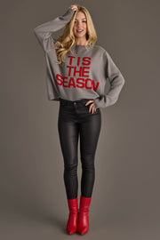 A woman wearing a Gray Tis The Season Sweater paired with black pants and red boots.