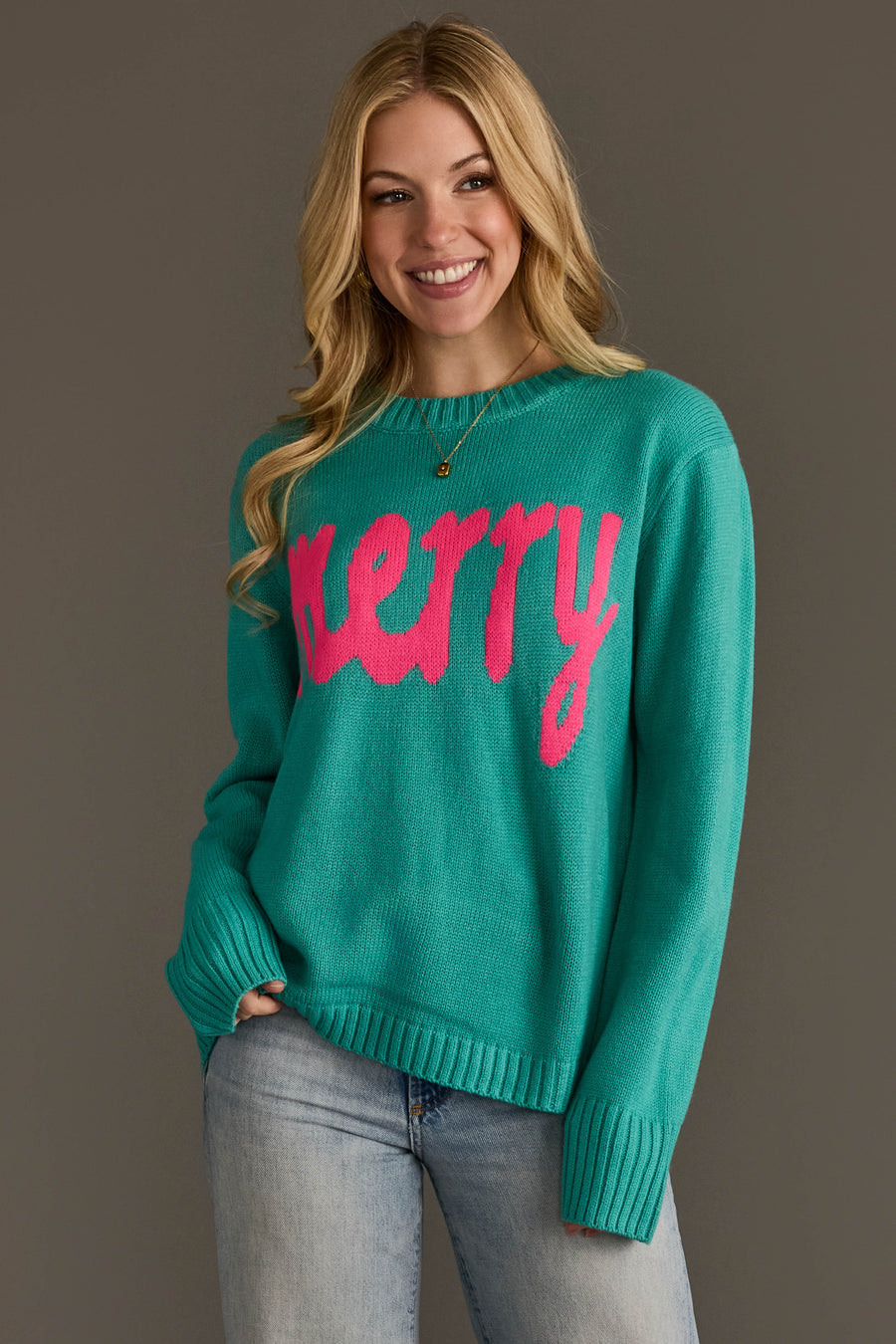 A woman wearing a Light Blue & Bright Pink Merry Sweater, featuring a teal crewneck with the word merry in bright pink script across the front.