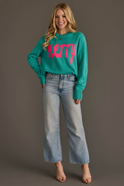 A smiling woman wears a Light Blue & Bright Pink Merry Sweater in bright teal with wide-leg light-wash jeans.