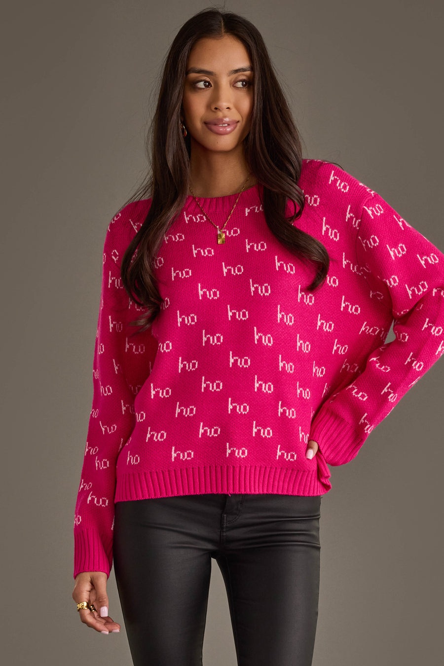 A woman wears a Bright Pink & Light Pink Ho Ho Ho Sweater featuring white ho ho ho text repeated across the bright pink fabric.