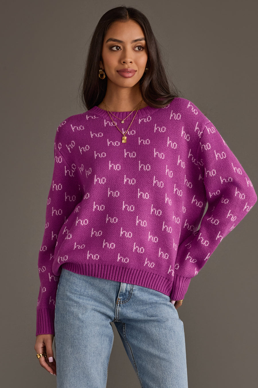 A person wearing a purple Purple Ho Ho Ho Sweater with a repeating white ho pattern, paired with blue jeans.