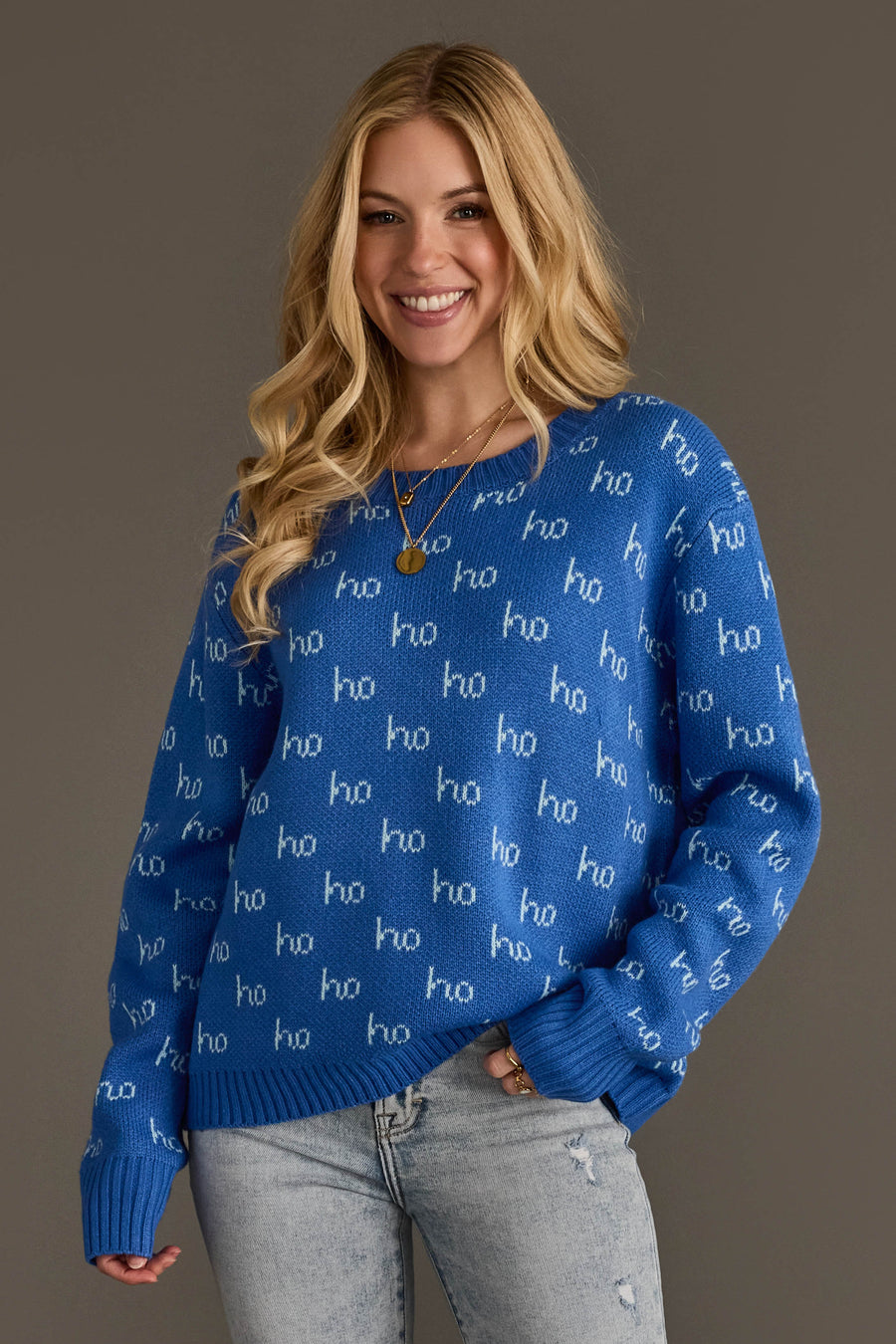 A smiling woman wearing a blue long-sleeved Blue Ho Ho Ho Sweater with a repeating white ho pattern.