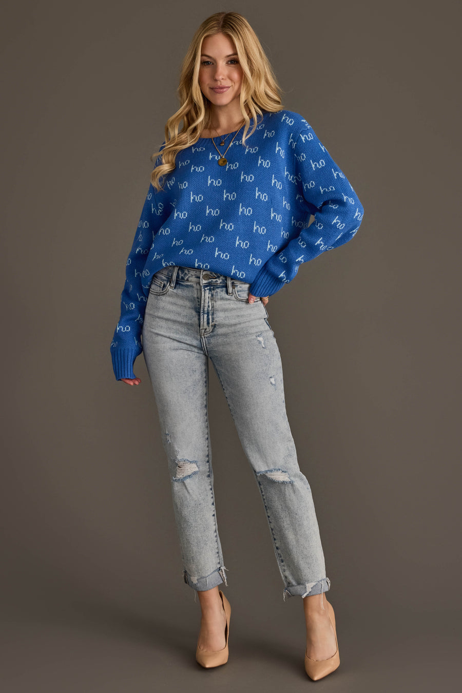 A woman wearing a Blue Ho Ho Ho Sweater with light-wash distressed jeans and tan heels.