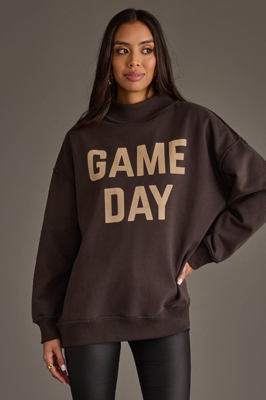 A woman models the Panache Apparel Collection’s Dark Gray Game Day & Sunday Funday Reversible Sweatshirt, featuring bold beige "GAME DAY" lettering on the front, paired with black pants, against a plain gray backdrop.
