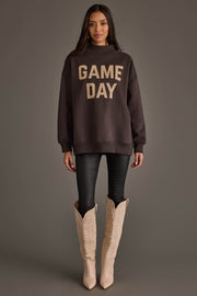 A woman stands facing forward against a plain gray background, wearing the Panache Apparel Collection's Dark Gray Game Day & Sunday Funday Reversible Sweatshirt, black leggings, and cream-colored cowboy boots.