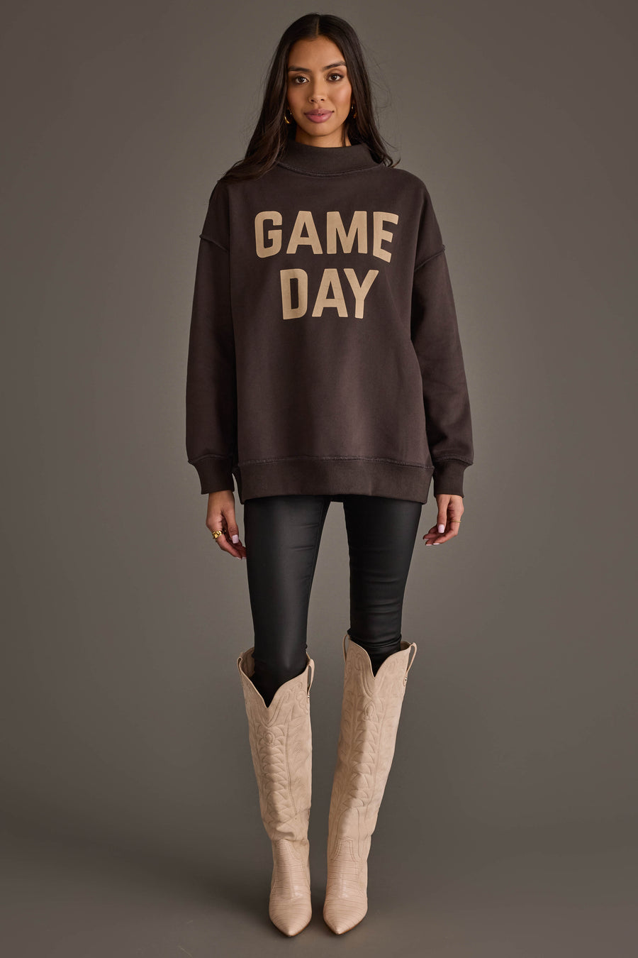 A woman stands facing forward against a plain gray background, wearing the Panache Apparel Collection's Dark Gray Game Day & Sunday Funday Reversible Sweatshirt, black leggings, and cream-colored cowboy boots.