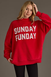 A woman smiles and touches her hair as she stands against a plain background, wearing the Panache Apparel Collection's Red Game Day & Sunday Funday Reversible Sweatshirt featuring bold white "SUNDAY FUNDAY" lettering.