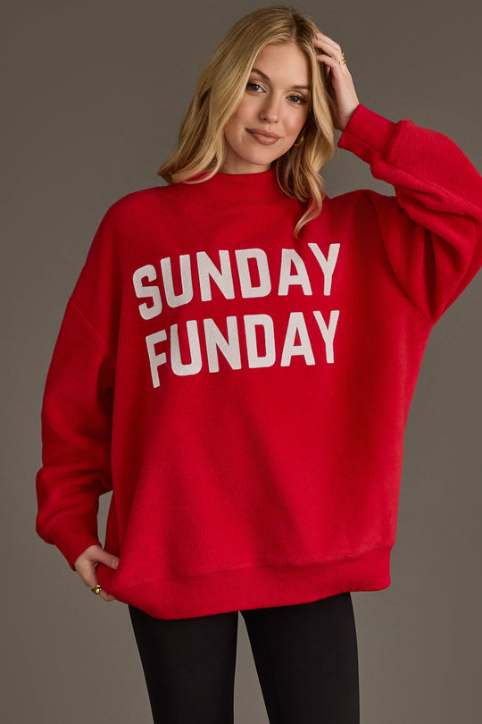 A woman smiles and touches her hair as she stands against a plain background, wearing the Panache Apparel Collection's Red Game Day & Sunday Funday Reversible Sweatshirt featuring bold white "SUNDAY FUNDAY" lettering.