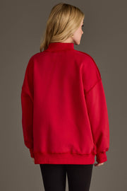 A woman with long blonde hair, seen from behind, wears the Panache Apparel Collection's Red Game Day & Sunday Funday Reversible Sweatshirt and black leggings against a plain, neutral background.