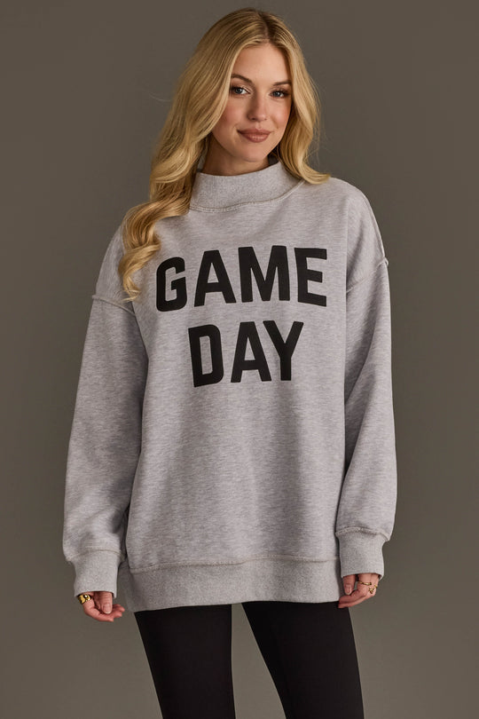 A woman with long blonde hair wears the Panache Apparel Collection Light Gray Game Day & Sunday Funday Reversible Sweatshirt, styled with black leggings, standing against a plain gray background.