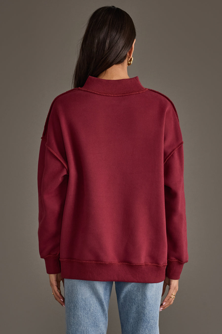 Back view of a person wearing a maroon high-neck Burgundy Wine & Prosecco Reversible Sweatshirt and blue jeans.