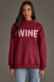 A person wearing a burgundy Wine & Prosecco Reversible Sweatshirt featuring a mock neck and the word WINE printed in light pink on the front.