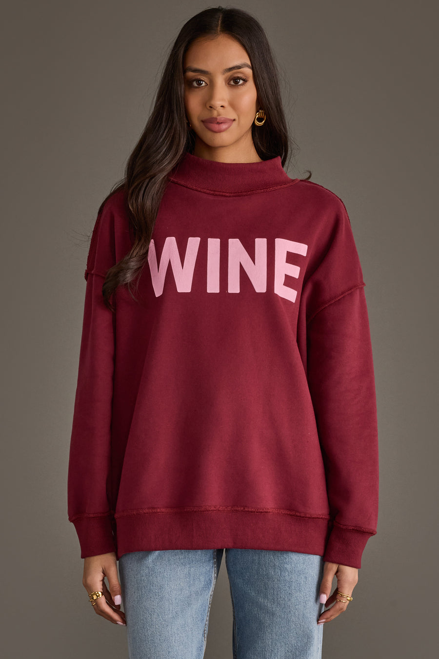 A person wearing a burgundy Wine & Prosecco Reversible Sweatshirt featuring a mock neck and the word WINE printed in light pink on the front.