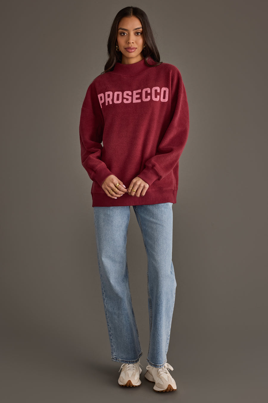 A person wearing a burgundy Burgundy Wine & Prosecco Reversible Sweatshirt with PROSECCO printed on the front, light-wash jeans, and athletic sneakers.