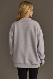 A person with long blonde hair, wearing the Panache Apparel Collection Light Gray Wine & Prosecco Reversible Sweatshirt and black leggings, stands facing away from the camera against a plain, dark background.