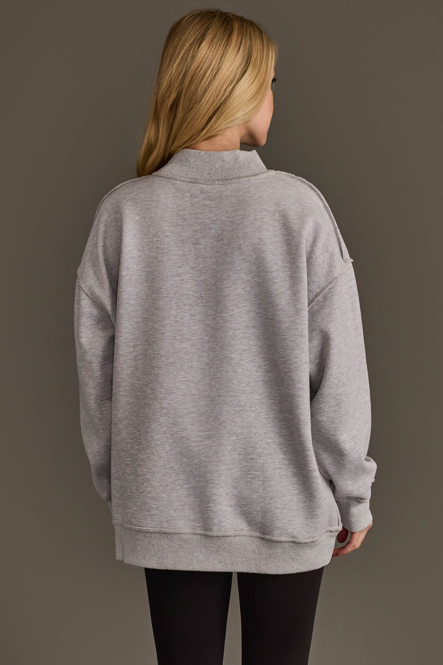 A person with long blonde hair, wearing the Panache Apparel Collection Light Gray Wine & Prosecco Reversible Sweatshirt and black leggings, stands facing away from the camera against a plain, dark background.