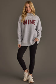 A woman with long blonde hair stands and poses against a plain brown background, wearing the Panache Apparel Collection Light Gray Wine & Prosecco Reversible Sweatshirt, paired with black leggings and beige sneakers.