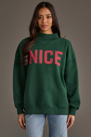 A person wearing a dark green Dark Green Nice & Naughty Reversible Sweatshirt with the word NICE printed in red on the chest.