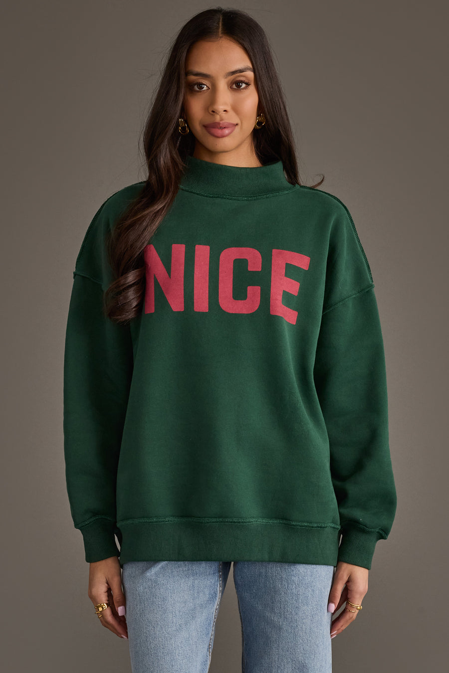 A person wearing a dark green Dark Green Nice & Naughty Reversible Sweatshirt with the word NICE printed in red on the chest.