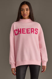 Pink Merry & Cheers Reversible Sweatshirt, a pink mock-neck design with the word CHEERS in dark pink letters across the chest.