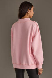 A person seen from behind wears a Pink Merry & Cheers Reversible Sweatshirt, a light pink, long-sleeved mock-neck top with exposed seam details.