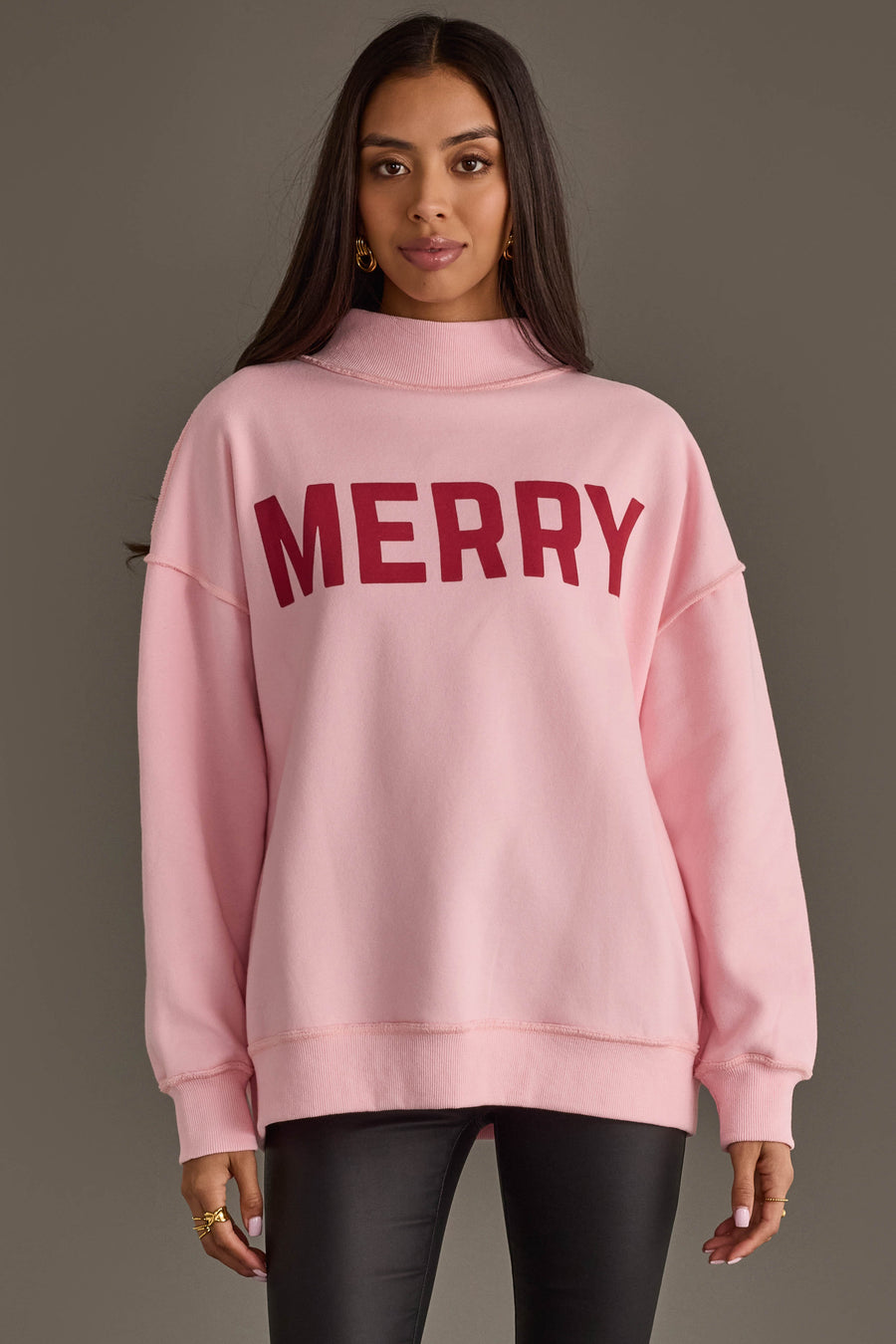 A person wearing a Pink Merry & Cheers Reversible Sweatshirt, a light pink mock-neck style with the word MERRY in large red letters on the chest.
