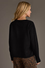 A woman with blonde hair models the Panache Apparel Collection's Black Football Season Sweater, paired with brown leopard print pants, as she stands facing away from the camera against a plain background.