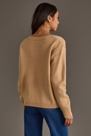 Wearing the Tan Football Season Sweater from Panache Apparel Collection, a woman with long dark hair, gold hoop earrings, and blue jeans stands facing away against a plain gray background.