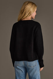 A woman with blonde hair, wearing the Panache Apparel Collection Black Football Sweater and light blue jeans, stands facing away from the camera against a plain, neutral background.