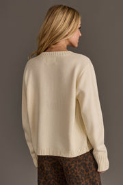 A woman with long blonde hair facing away, wearing the Ivory Football Mom Sweater from Panache Apparel Collection and brown leopard-print pants, stands against a plain gray background.