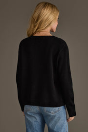 A person with long blonde hair, wearing the Black & Tan Football Mom Sweater from Panache Apparel Collection and blue jeans, stands facing away from the camera against a plain background.