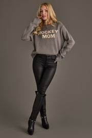 A person with long blonde hair wears the Panache Apparel Collection Gray Hockey Mom Sweater, paired with black pants and black knee-high boots, posing against a plain gray background.