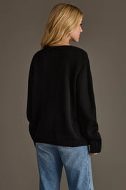 A person with blonde hair, seen from behind, wearing the Black Coffee Weather Sweater by Panache Apparel Collection and blue jeans, stands in front of a plain brown background.