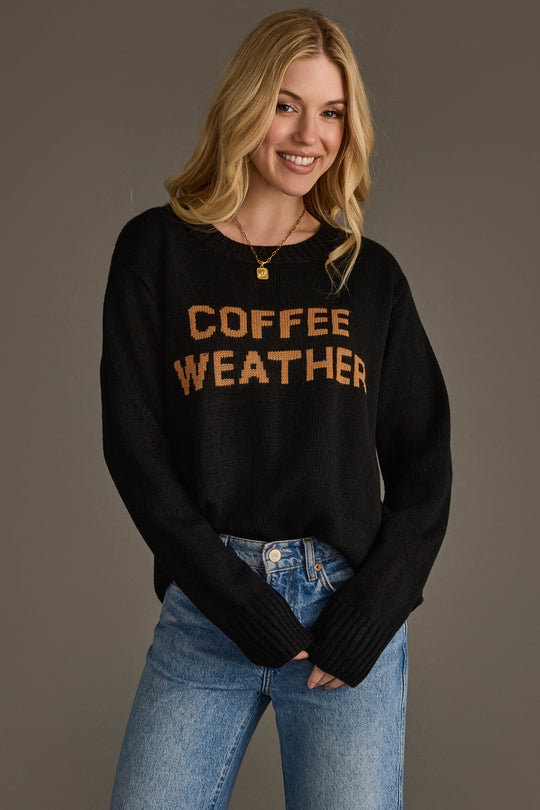 A woman stands smiling against a plain background, wearing the Panache Apparel Collection Black Coffee Weather Sweater paired with blue jeans.