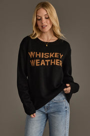 A person with long blonde hair wears the Panache Apparel Collection Black & Tan Whiskey Weather Sweater and blue jeans, standing against a plain gray background.