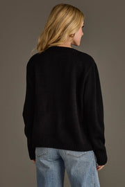 A person with shoulder-length blonde hair is wearing the Beer Weather Sweater from Panache Apparel Collection and light blue jeans, standing against a plain grey background and facing away from the camera.