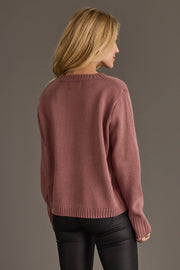 A woman with long blonde hair, seen from behind, wears the Mauve & White Wine Season Sweater by Panache Apparel Collection paired with black pants against a plain gray background.