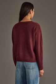 A woman with long brown hair models the Panache Apparel Collection's Burgundy & Light Pink Wine Season Sweater, paired with light blue jeans, as she stands facing away from the camera against a plain brown background.