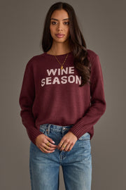 A woman with long dark hair is wearing the Panache Apparel Collection Burgundy & Light Pink Wine Season Sweater and blue jeans, standing against a gray background.