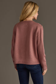 A woman with blonde hair, seen from behind, models the Panache Apparel Collection’s Mauve & White Wine Sweater paired with dark blue jeans against a plain, neutral background.
