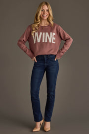 A woman stands smiling, wearing the Mauve & White Wine Sweater from Panache Apparel Collection, paired with dark blue jeans and tan heels. She has long blonde hair and poses with her hands on her hips against a plain background.