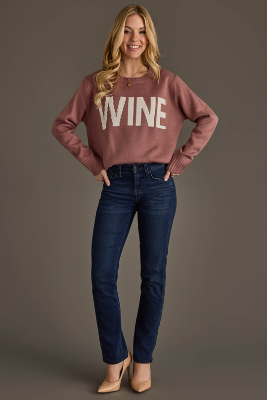 A woman stands smiling, wearing the Mauve & White Wine Sweater from Panache Apparel Collection, paired with dark blue jeans and tan heels. She has long blonde hair and poses with her hands on her hips against a plain background.