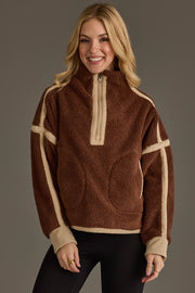 A smiling woman with long blonde hair wears the Brown & Tan Half Zip Sherpa Fleece Sweatshirt by Panache Apparel Collection and black pants, standing against a plain gray background.