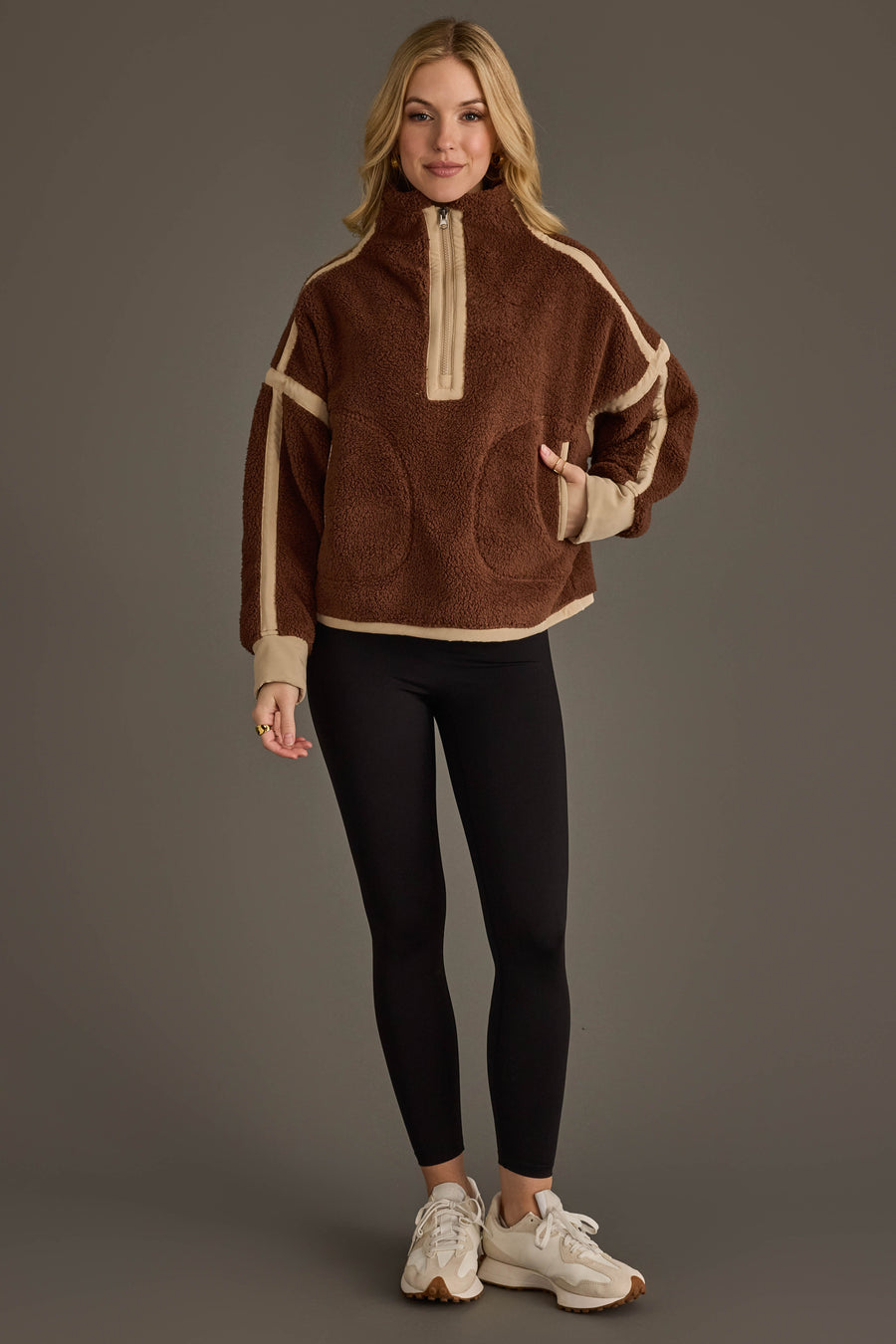 A person wearing the Panache Apparel Collection Brown & Tan Half Zip Sherpa Fleece Sweatshirt, paired with black leggings and white sneakers, stands against a plain gray background.