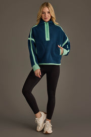 A woman stands and smiles, wearing the Panache Apparel Collection Navy & Mint Half Zip Sherpa Fleece Sweatshirt, paired with black leggings and white sneakers, as she poses against a plain gray background.