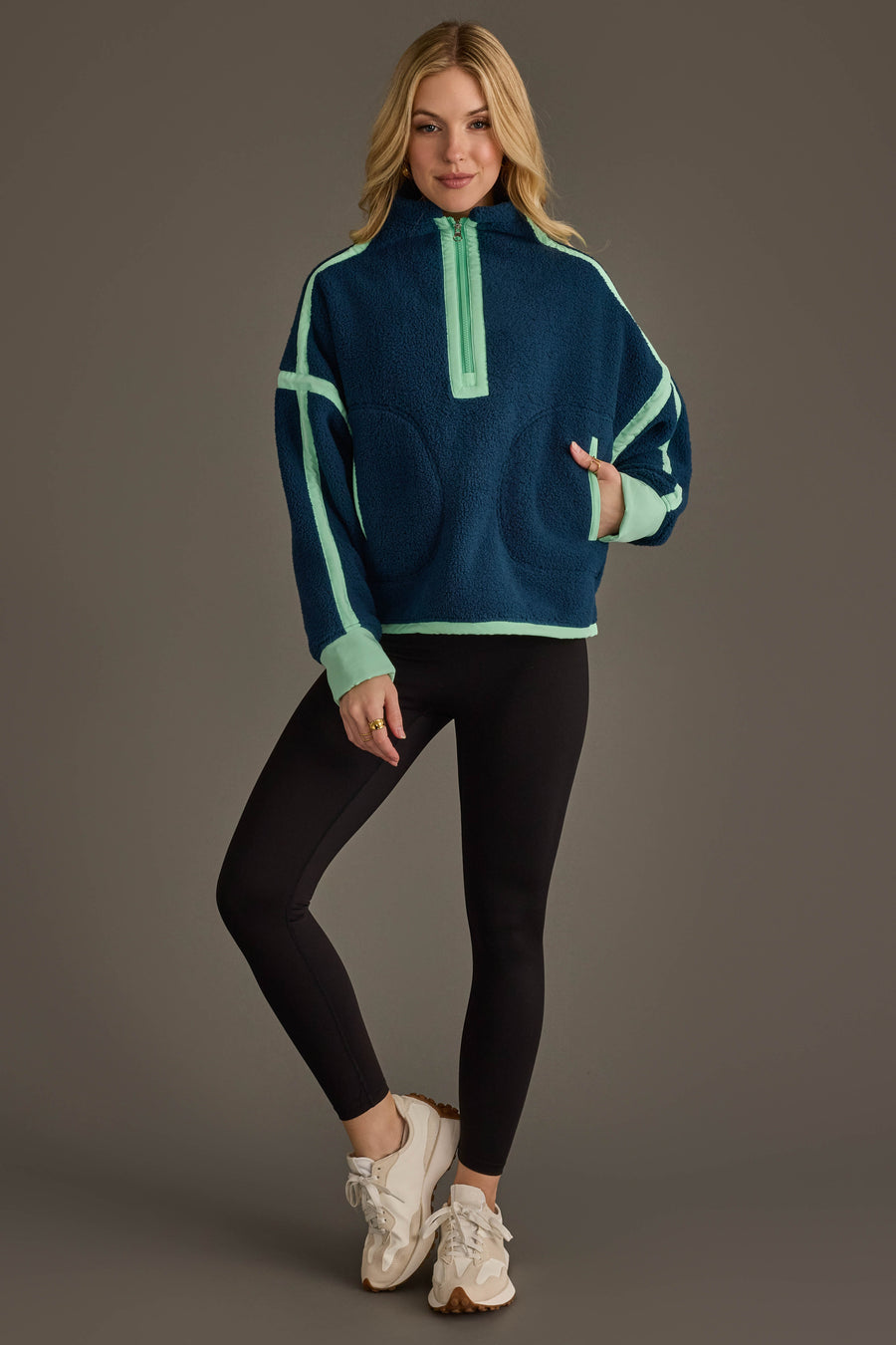 A woman stands and smiles, wearing the Panache Apparel Collection Navy & Mint Half Zip Sherpa Fleece Sweatshirt, paired with black leggings and white sneakers, as she poses against a plain gray background.